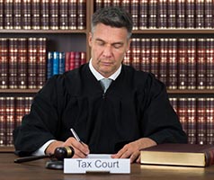 Judge signing document. Tax Court sign on desk.