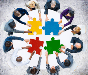 People in circle holding large puzzle pieces.
