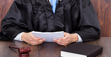 Judge holding a stack of papers. Book and gavel nearby.