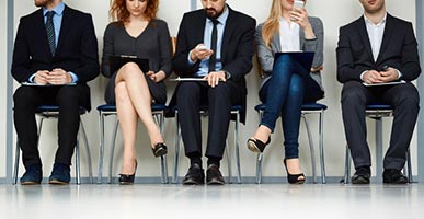 Line of people sitting by wall while waiting for their turn for interview