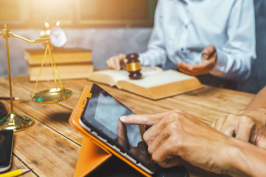 One person with gavel, another person with only hands visible on an ipad