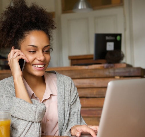 Woman with phone to ear while looking at her laptop