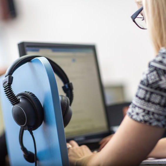 A person working at a computer with headphones hanging on the monitor.